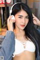 A woman in a white bra top and denim jacket listening to music.