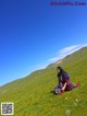 A woman sitting on a grassy hill in a field.