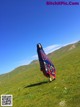 A woman standing in a grassy field with mountains in the background.