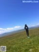 A woman standing in a field of flowers with mountains in the background.