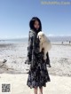 A woman holding a small white dog on a beach.