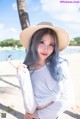 A woman with blue hair wearing a straw hat on the beach.