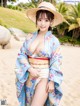 A woman in a blue kimono and a straw hat on a beach.