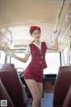 A woman in a red uniform is standing on a bus.