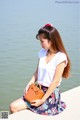 A woman sitting on the edge of a body of water holding a brown bag.