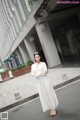 A woman in a white dress is standing on the street.