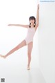 A young girl in a pink leotard leaning against a wall.