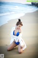 A woman in a blue bikini sitting on the beach.