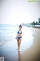 A woman in a blue bikini walking on the beach.