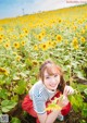 A woman kneeling in a field of sunflowers holding a flower.