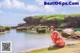 A woman in a red kimono sitting on the edge of a body of water.