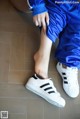 A woman in a blue tracksuit and white sneakers sitting on the floor.