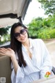 A woman in a white shirt and sunglasses sitting in a car.