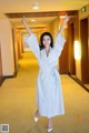 A woman in a white robe standing in a hallway.