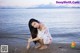 A woman in a white dress crouching on the beach.