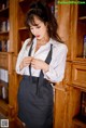 A woman in a white shirt and black skirt standing in front of a bookcase.