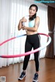 A woman in a blue top and black leggings holding a hula hoop.