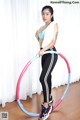 A woman in a blue top and black leggings is holding a hula hoop.