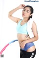 A woman in a blue sports bra top and black shorts holding a pink hula hoop.