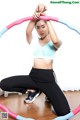 A woman in a blue sports bra top and black leggings holding a hula hoop.