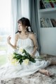 A woman in a white dress sitting on a rug holding a bouquet of flowers.