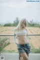 A woman in a white top and denim shorts posing for a picture.