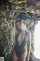 A woman in a gray swimsuit posing in front of a rock.