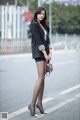 A woman in a black blazer and polka dot tights is standing on the street.