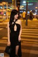 A woman in a black dress standing on a city street at night.