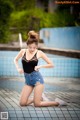 A woman in a black top and denim shorts by a swimming pool.