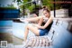 A woman sitting on a bench next to a swimming pool.