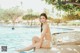 A woman in a blue bikini sitting by a swimming pool.