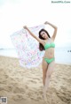 A woman in a green bikini holding a colorful scarf on the beach.