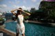 A woman in a white dress standing next to a swimming pool.