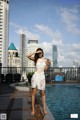 A woman in a white dress standing next to a swimming pool.