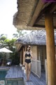 A woman in a black bikini standing on a wooden deck next to a pool.