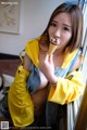 A woman in a yellow hoodie eating an ice cream cone.