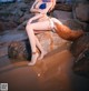 A woman in a bikini sitting on a rock on the beach.