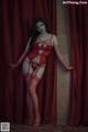 A woman in a red lingerie posing in front of a red curtain.