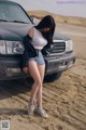 A woman standing next to a car in the desert.