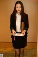 A woman in a black skirt and a white shirt holding a book.