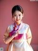 A woman in a pink and white hanbok poses for a picture.