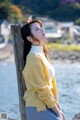 A woman leaning against a wooden post by the water.