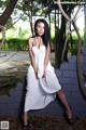 A woman in a white dress sitting on a brick wall.