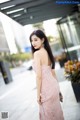 A woman in a pink dress standing on a sidewalk.