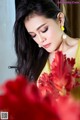 A woman in a yellow dress holding a bunch of red flowers.