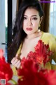 A woman in a yellow dress holding a bunch of red flowers.