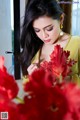 A woman in a yellow dress smelling red flowers.