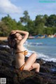 A woman in an orange bikini sitting on a rock by the ocean.