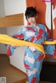 A woman in a blue and red kimono holding a yellow scarf.